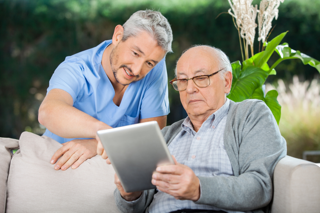 Male caretaker assisting senior man in using digital tablet at n